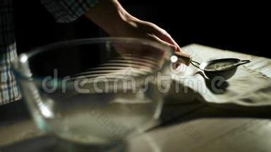 人用手把面粉通过筛子倒入玻璃碗里。 食品成分